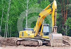 Yellow excavator with a crawler on a caterpillar track, works on the construction of a highway