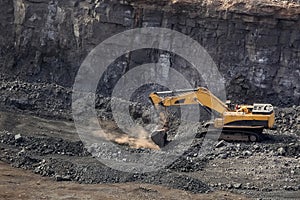 Yellow excavator digging for ore rich rock in an open pit mine