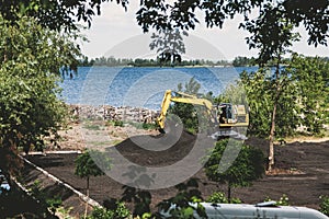 Yellow excavator digs soil on river bank