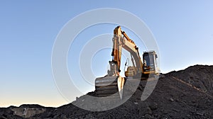 Yellow excavator during earthmoving at open pit on blue sky background. Construction machinery and earth-moving heavy equipment