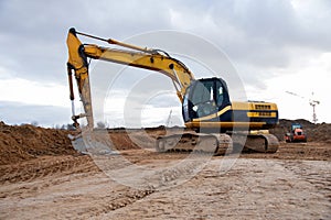 Yellow excavator during earthworks at construction site. Backhoe digging the ground for the foundation and for laying sewer pipes