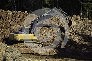 Yellow excavator during earthworks in an open pit against the background of forest and soil