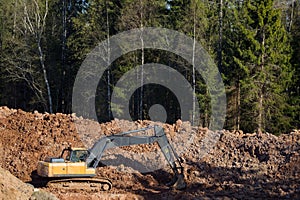 Yellow excavator during earthworks in an open pit against the background of forest and soil