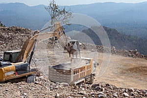 Yellow excavator is filling a dump truck with rocks at coal mines