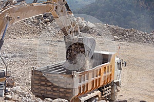 Yellow excavator is filling a dump truck with rocks at coal mines