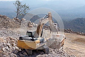 Yellow excavator is filling a dump truck with rocks at coal mines