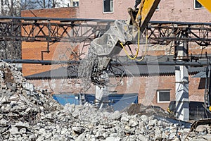 A yellow excavator with a hydraulic concrete pulverizer lifts a pile of old metal reinforcing bars over a pile of