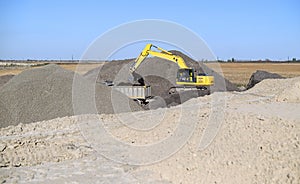 Yellow excavator involved in the construction of a highway loading rubble into a truck