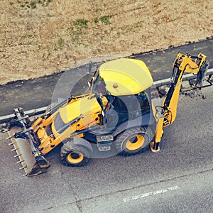 Yellow excavator with jackhammer removes asphalt from the road