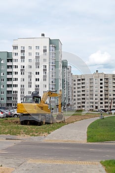 Yellow excavator levels the lawn area. Improvement of a new residential area