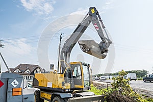 Yellow excavator loader standing against sunny cloudy sky during road construction and repairing asphalt pavement works.