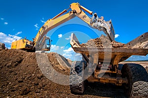 Yellow excavator loading soil into a dumper truck