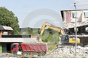 Yellow excavator loads construction debris into the truck. Technique destroys the building, is fittings, concrete and stones.