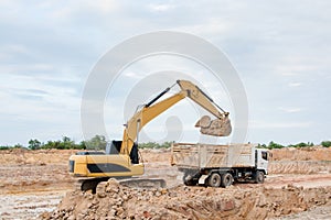 Yellow excavator machine loading soil into a dump truck at construction site