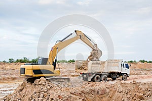 Yellow excavator machine loading soil into a dump truck at construction site