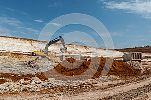 Yellow excavator mines clay and loads into grey truck.