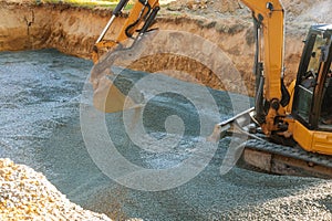 A yellow excavator moving gravel in the foundation in the house