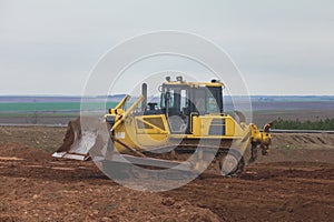 Yellow excavator on a road construction site among fields