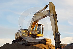 Yellow excavator on sandpile in construction site