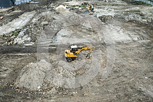 Yellow excavator standing on a ground during construction of a new building in the city area. Aerial view on a