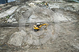 Yellow excavator standing on a ground during construction of a new building in the city area. Aerial view on a photo