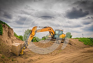 yellow excavator stands on a mound of earth on a large construction site