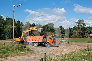 Yellow excavator working on clearing the rubble. Puts the earth into a dump truck on a Sunny day.