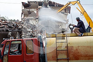 A yellow excavator is working on demolishing an old house in the city of Alanya, Turkey