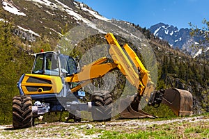 Yellow excavator working near mountains