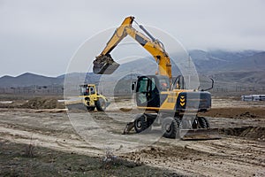 Yellow excavator works against the background of mountains