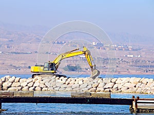 Yellow excavator works on breakwater