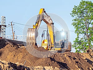 A yellow excavator works on a construction site. Earthworks in the city. Digging a pit