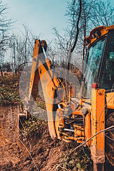 A yellow excavator works on the forest clearing and digs soil