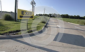 Yellow exit sign outdoors pointing towards an empty roadway