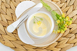 Yellow facial mask (face cream, body butter, hair conditioner) in a small white container and linden flowers.