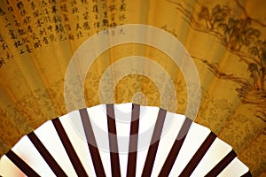 Yellow fan with brown chinese characters on it, white background, closeup