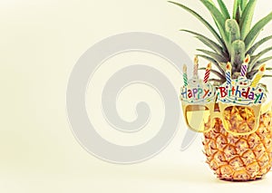 Yellow fancy glasses on fresh pineapple, copy space on left, summer birthday concept, pastel color