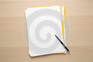 Yellow file with blank sheets of paper and pen on wooden table, top view. Space for design