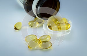 Yellow fish oil pills spilling out of a drug bottle, isolated on blue background