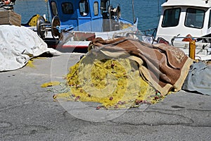 Yellow fishing net with red-brown floats piled on pavement in port of Heraklion.