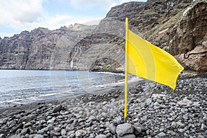 Yellow flag on a Black volcanic beach. Selective focus. Los Gigantes, Tenerife