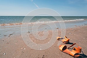 Yellow flip flop on the beach. Summer holidays concept. Sandals, sand, sea, blue sky with bright light of sunset in summer