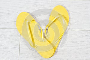 Yellow flip-flops on a white wooden background close up