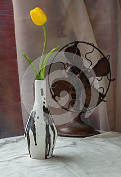 Yellow flower in Black and White Handmade ceramic vase and Vintage fan on white textured table cloth with old cement wall