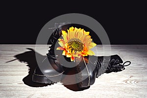 Yellow flower on leather black boots on a wooden surface