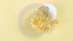 Yellow flowers in an egg shell on a yellow background. Copy space