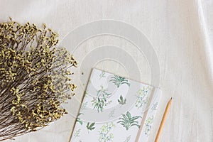 Yellow flowers with notebook and pencil over the white fabric.