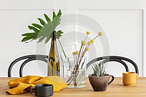 Yellow flowers in vase, a bottle of wine, washcloth and coffee cup on wooden dining table