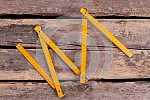 Yellow folding ruler on wooden boards background.