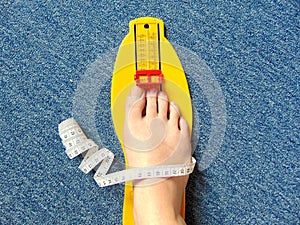 Yellow foot measurement device with naked foot upon with measuring tape